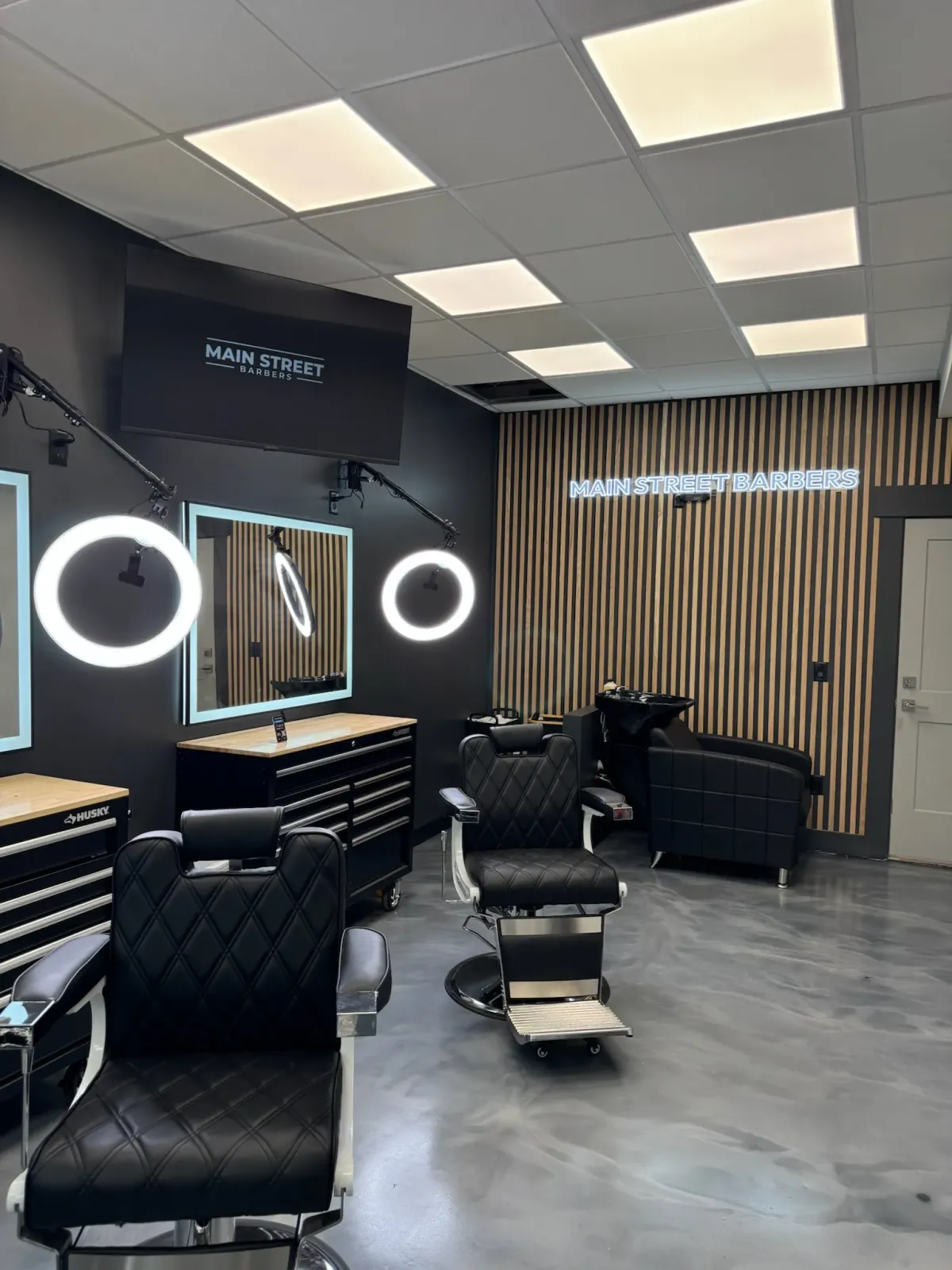 Inside Main Street Barbers — empty booths with leather chairs, ring-light mirrors, and slat-wall accent.